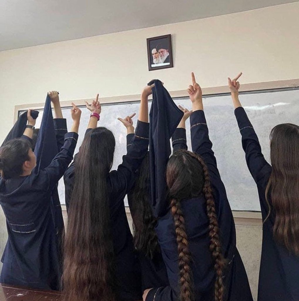 Les filles iraniennes font un doigt et retirent leur voile devant les portraits des ayatollahs accroché au dessus de leur tableau